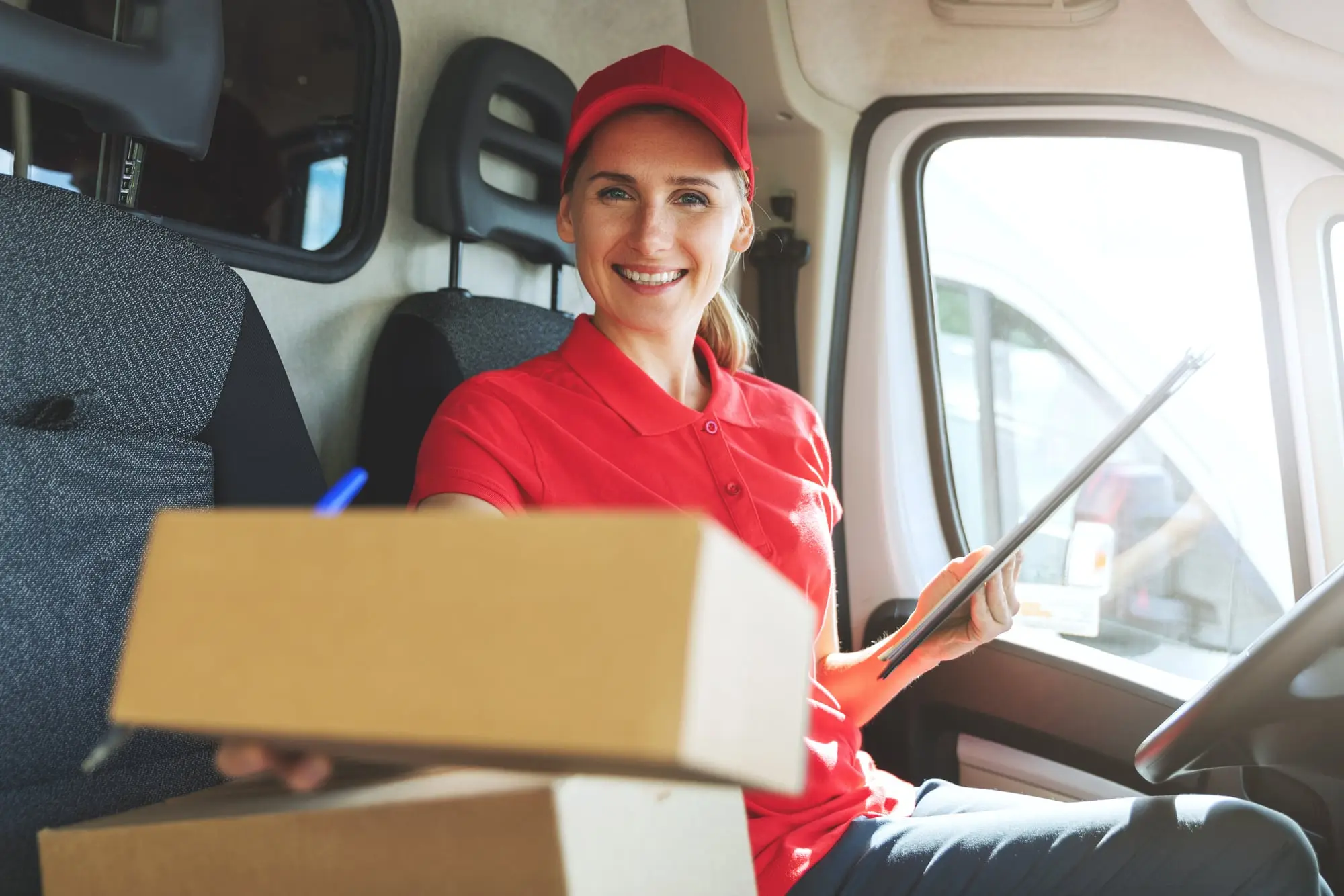 A courier in her delivery van, smiling and holding out a parcel