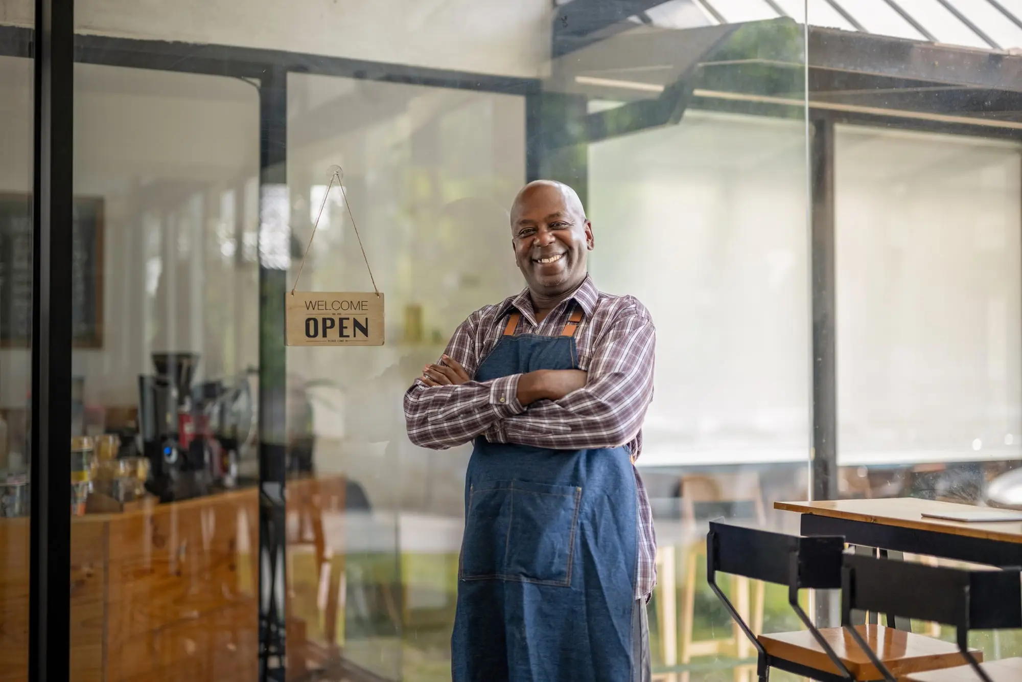 A small-business owner standing in the doorway of his shop, arms crossed, beside an Open sign